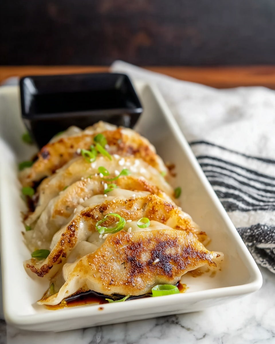 A white rectangular dish holds four pan-fried dumplings arranged in a single row, each with a crispy golden-brown bottom and slightly translucent, soft dough on top. The dumplings are lightly garnished with small green onion slices and a few sesame seeds scattered on and around them. Behind the dumplings, a small black square container filled with dark soy sauce sits at the back of the dish. The dish rests on a white marbled surface with a blurred dark background and a white cloth with black stripes folded nearby. Photo taken with an iphone --ar 4:5 --v 7