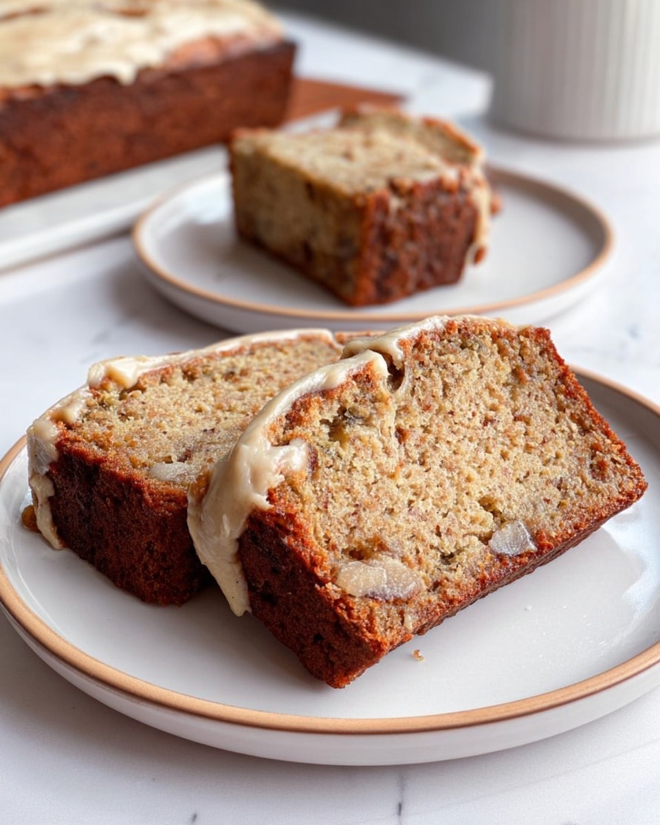 A thick loaf cake is sliced into even pieces and sits on a white plate with a light pink rim. The cake has a deep brown outer crust with a textured, moist interior that shows bits of nuts or fruit. On top of each slice, there is a thick layer of creamy off-white frosting, generously spread and slightly draped over the edges, dusted evenly with a light brown powder, likely cinnamon or nutmeg. The cake rests on a white marbled surface near a window with soft natural light coming in. Photo taken with an iphone --ar 4:5 --v 7