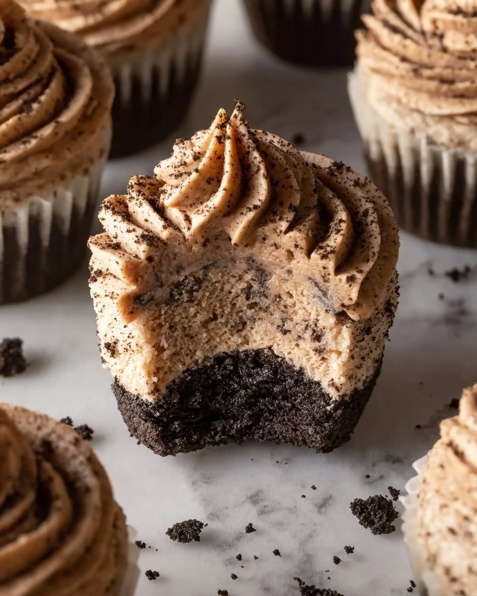 A close-up view of a cupcake with three visible layers: the bottom layer is a dark cookie crumb base, the middle layer is a light beige creamy batter mixed with dark cookie bits, and the top layer is a swirl of light brown chocolate frosting with a textured, piped pattern. Around this cupcake, there are additional cupcakes with the same frosting style, all set on a white marbled surface with small cookie crumbs scattered around. photo taken with an iphone --ar 4:5 --v 7
