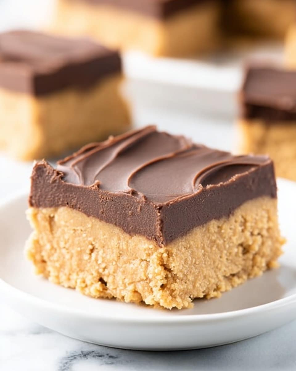 The image shows a close-up of a square dessert with two layers on a white plate resting on a white marbled surface. The bottom layer is thick and beige with a smooth yet slightly crumbly texture, resembling a peanut butter base. The top layer is a thinner, smooth dark brown chocolate frosting with a glossy finish and subtle swirls. In the background, more pieces of the dessert and a white plate are slightly out of focus. Photo taken with an iphone --ar 4:5 --v 7