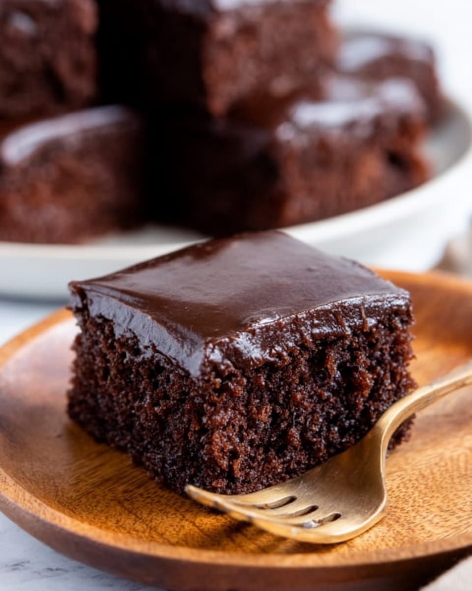 A square piece of rich chocolate cake with a smooth, shiny dark chocolate layer on top sits on a round wooden plate. The cake looks soft and moist, with a crumbly texture on the sides. A gold fork rests next to the cake on the plate. In the background, slightly out of focus, there is a white round plate piled with more pieces of the same chocolate cake. All of this is set on a white marbled surface. photo taken with an iphone --ar 4:5 --v 7
