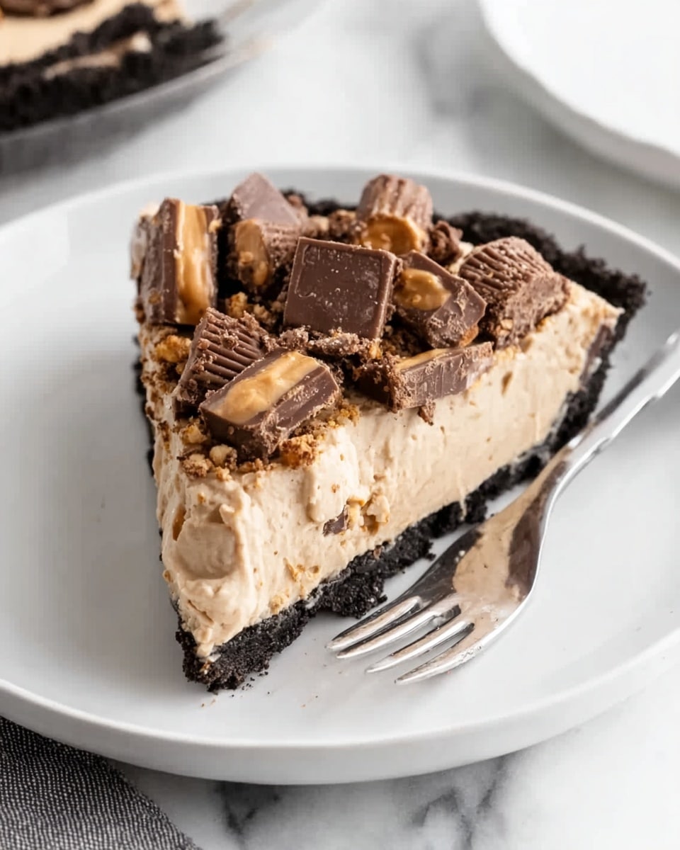 A slice of pie with three distinct layers is placed on a white plate against a white marbled surface. The bottom layer is a dark, crumbly crust, followed by a thick, creamy middle layer that is light brown and smooth in texture. The top layer is decorated with chunks of chocolate and peanut butter cups, adding a rough and uneven texture with dark and light brown colors. A silver fork rests on the plate beside the slice. Photo taken with an iphone --ar 4:5 --v 7