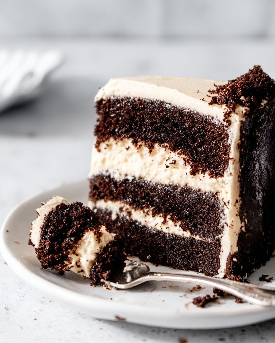 A close-up of a slice of chocolate layer cake on a white plate with a silver fork holding a small piece of cake. The cake has three layers: two thick layers of dark, moist chocolate cake with a crumbly texture, separated by a thick layer of smooth, white cream frosting. The frosting also covers the top and sides of the slice, showing some crumbs stuck to it. The plate rests on a white marbled surface with soft, natural lighting. Photo taken with an iphone --ar 4:5 --v 7