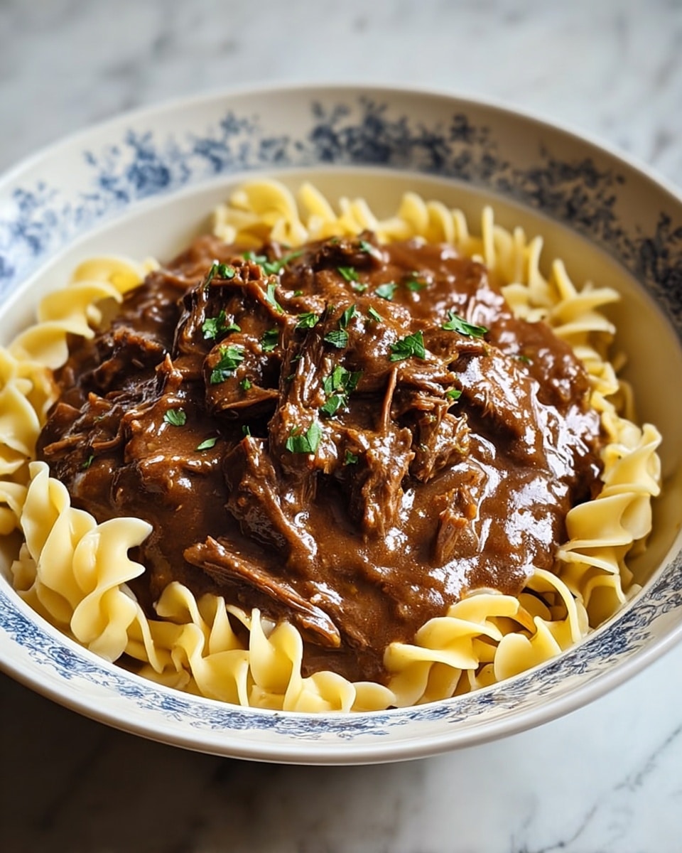 A white bowl with a blue floral pattern holds a layer of light yellow wide egg noodles arranged in a circular shape at the bottom. On top of the noodles, there is a thick layer of shredded beef covered in rich brown gravy with a smooth, glossy texture. Small pieces of green herbs are sprinkled over the beef as a garnish. The bowl is placed on a surface with a white marbled texture. photo taken with an iphone --ar 4:5 --v 7