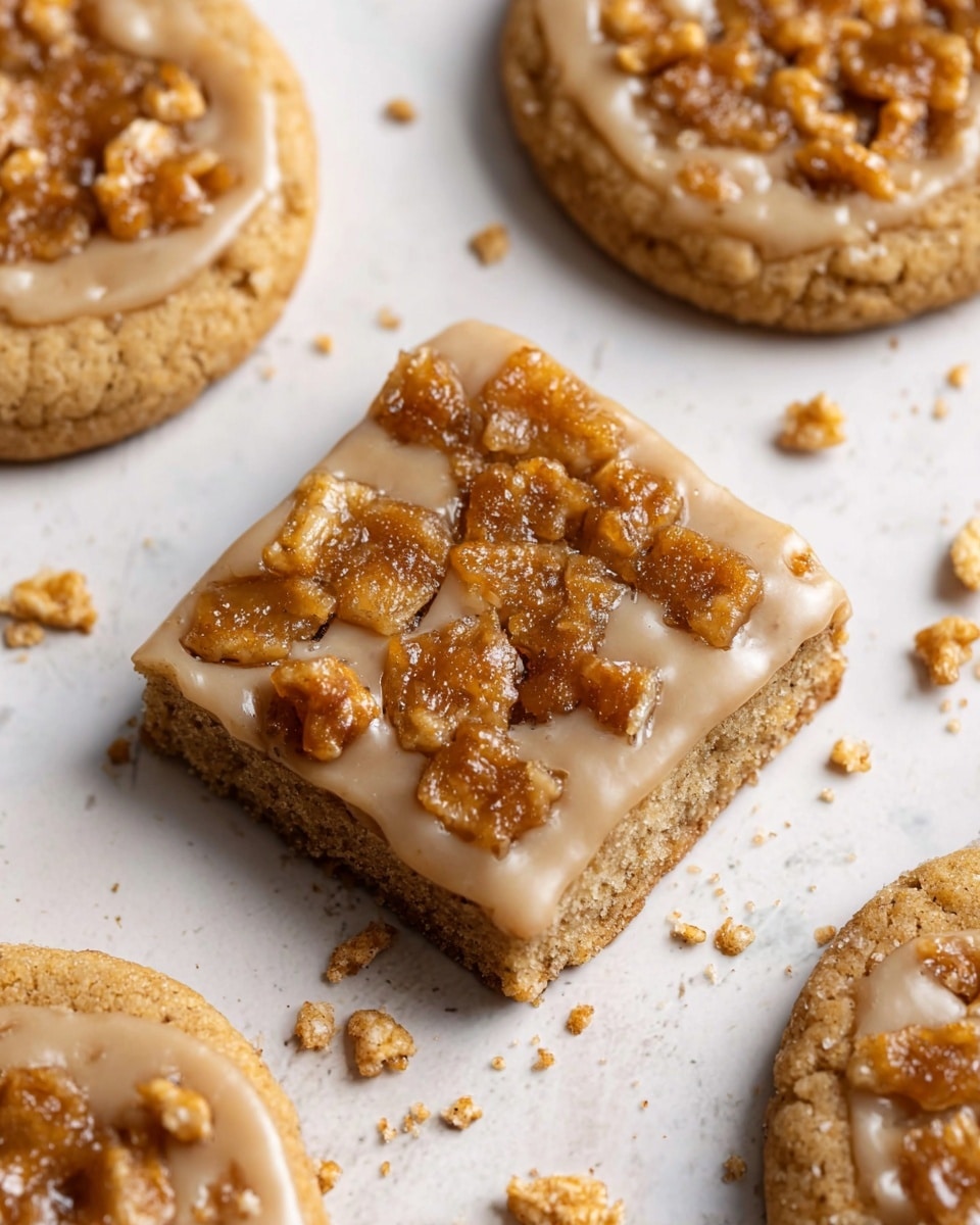 The image shows a close-up of several round cookies, each with three layers: a light brown base cookie with a soft, slightly crumbly texture, a thin off-white glaze layer spread evenly on top, and a topping of small, rough, golden-brown crunchy pieces scattered across the surface. The cookies are placed on a white marbled surface, with some crumbs spread around them, adding texture and detail to the scene. The cookies are arranged without overlapping, filling the frame with a warm, inviting look. photo taken with an iphone --ar 4:5 --v 7