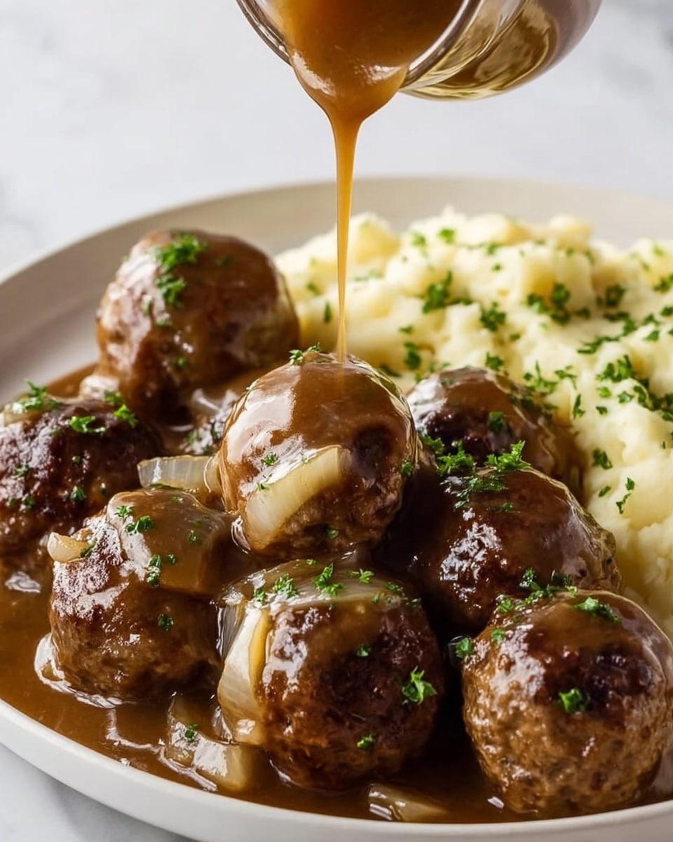The image shows a close-up of a white plate filled with several round, brown meatballs covered in a thick, glossy brown gravy with visible small onion slices mixed in. Bright green parsley is sprinkled over the meatballs for a fresh look. Behind the meatballs is a serving of creamy mashed potatoes with small green parsley pieces on top. A woman's hand is pouring more thick brown gravy from above onto the meatballs. The plate sits on a white marbled surface with a soft, clean background. photo taken with an iphone --ar 4:5 --v 7
