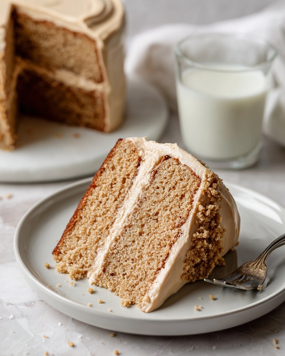 The image shows a slice of two-layer light brown cake on a white plate. Both cake layers have a soft, crumbly texture. Between the layers, there is a thick middle layer of smooth, creamy frosting in a light tan color. The same frosting covers the sides and top of the cake slice, with a few small crumbs pressed into the frosting on the side. In the background, there is a clear glass of milk, and the setting has a white marbled texture. A silver fork lies next to the plate, and a woman’s hand is gently holding the edge of the plate. photo taken with an iphone --ar 4:5 --v 7