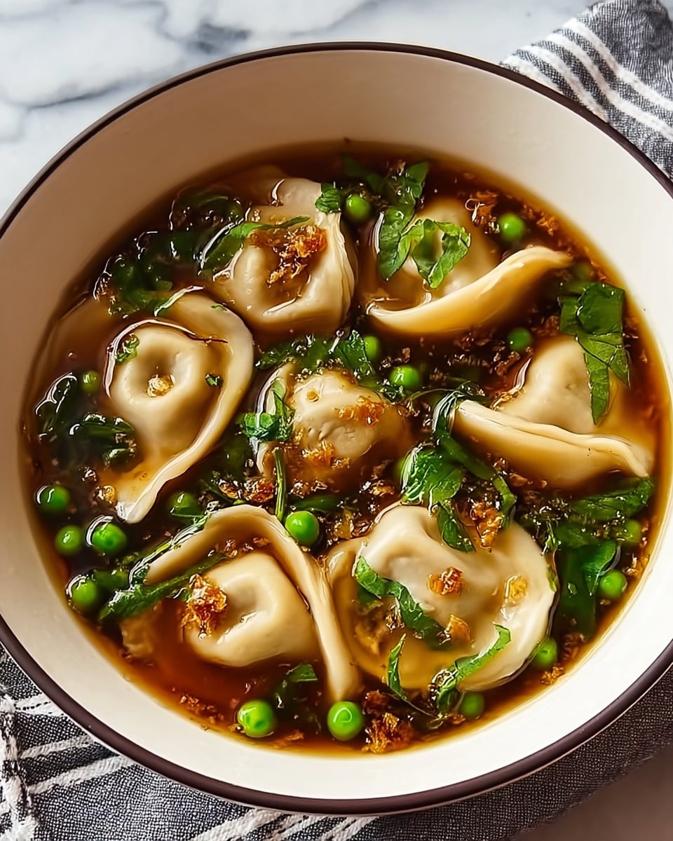 A white bowl with a thin dark rim holds a clear broth with a rich brown color. Inside the broth float soft, light beige dumplings with folded edges, some slightly curled. Scattered around the dumplings are bright green peas and dark green leafy herbs, adding contrast. Tiny bits of golden brown fried garlic or onions rest on top of the dumplings and in the broth, creating texture. The bowl sits on a white marbled surface with a striped cloth partially visible beneath it. Photo taken with an iphone --ar 4:5 --v 7