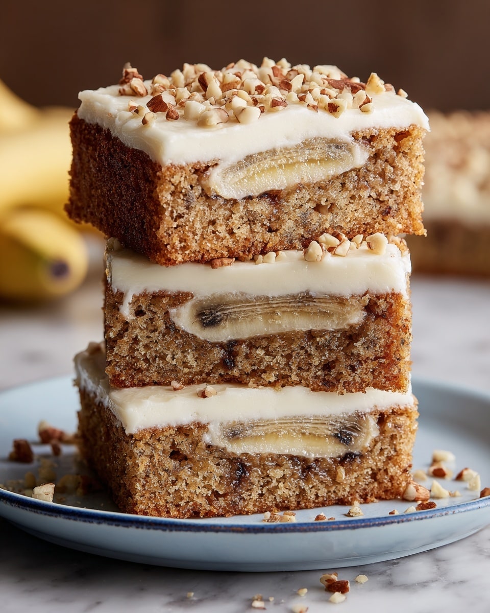 Three square slices of banana cake are stacked on top of each other on a white plate with a blue rim, placed on a white marbled surface. Each slice has one layer of light brown moist cake containing a banana piece in the middle and small dark spots, likely chocolate or nuts, visible inside. On top of each cake slice is a thick, smooth layer of creamy white frosting sprinkled with small chopped nuts. The top slice shows the texture of the cake and the banana clearly, while the crumbs and nut pieces are scattered on the plate around the cake stack. photo taken with an iphone --ar 4:5 --v 7